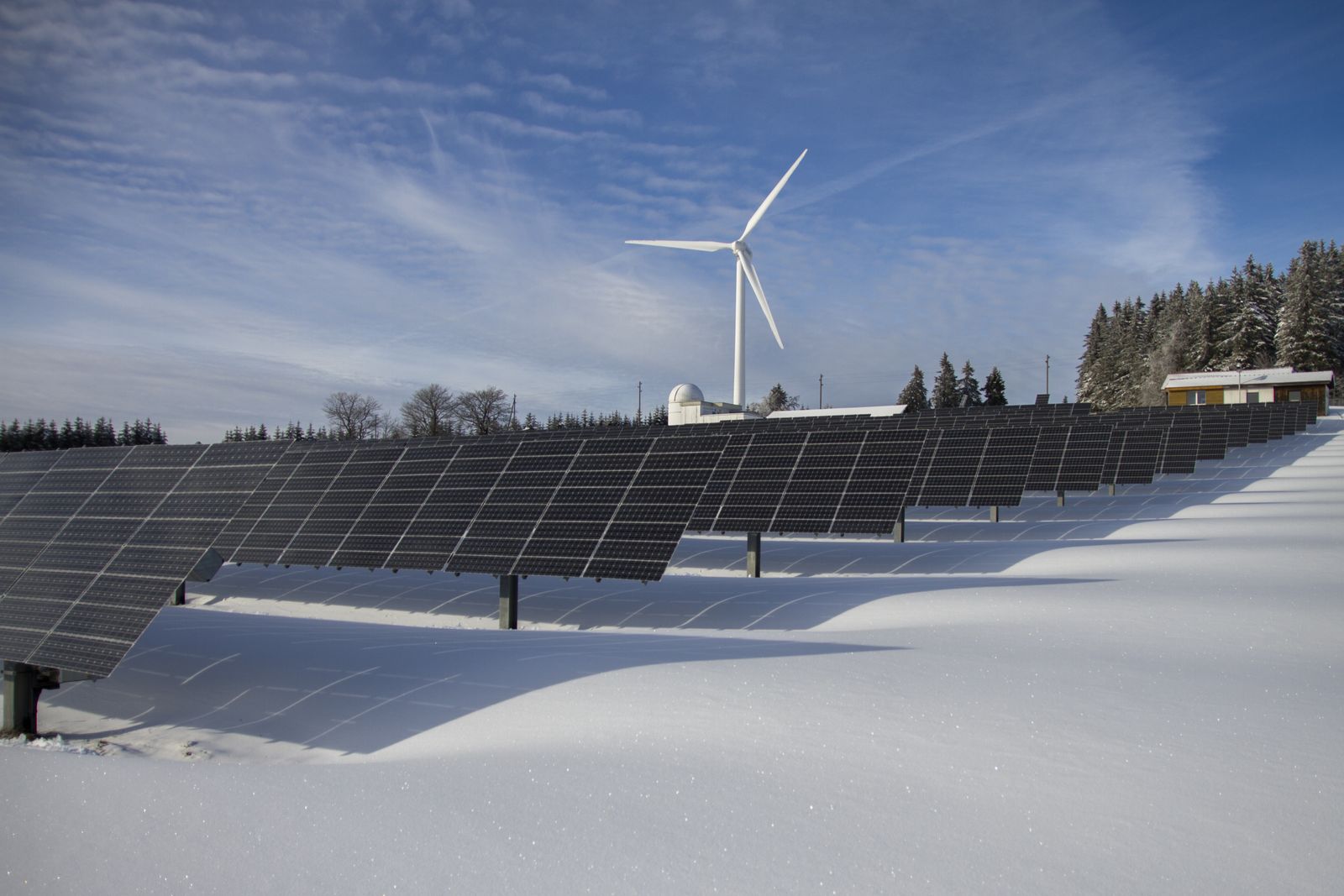 Solarpark im Schnee vor Windrad — erneuerbare Energie im alpinen Winter