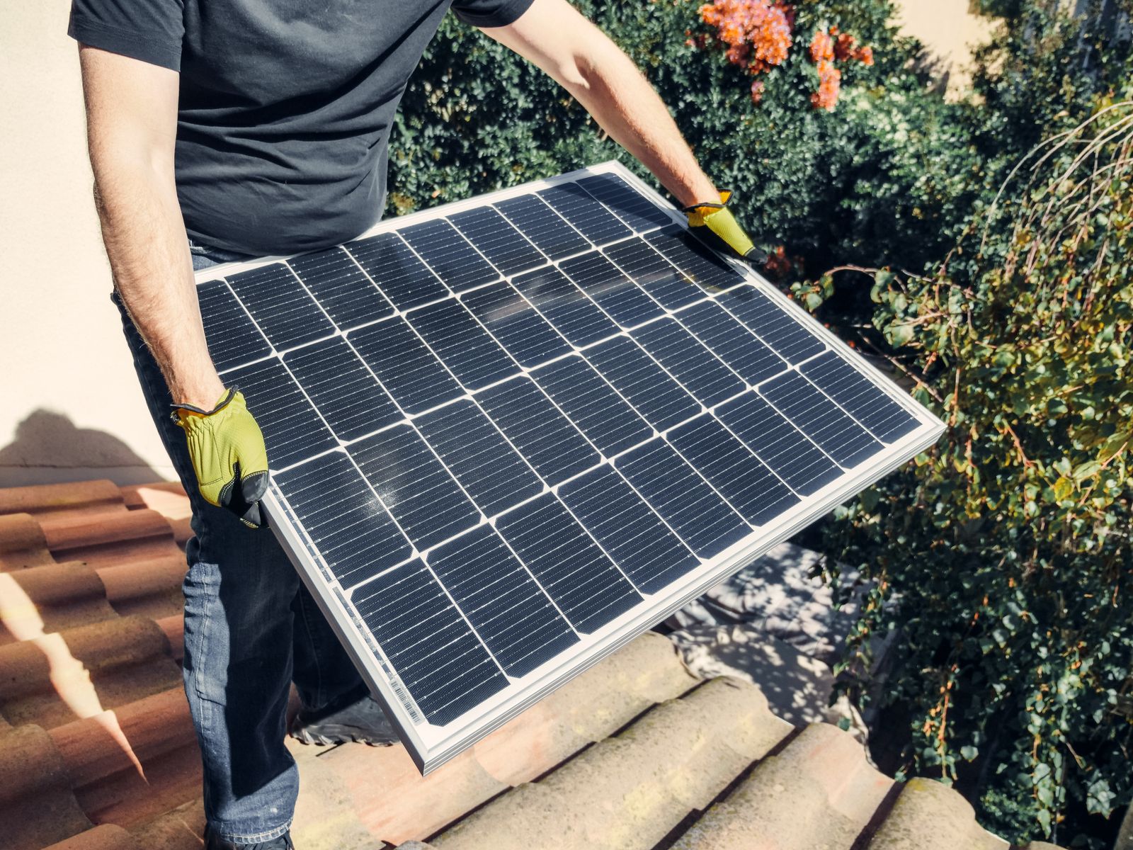Monteur trägt ein Photovoltaik-Modul auf ein Ziegeldach